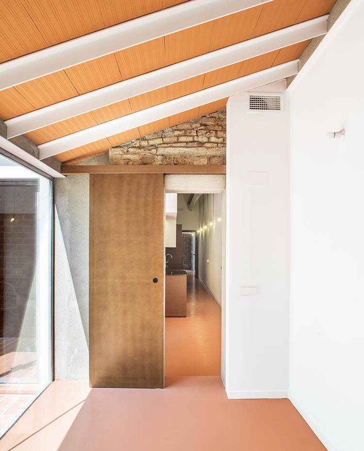 Zona de paso, puerta corredera de madera, pared blanca con detalle obra vista. La puerta corredera de la estancia polivalente está pensada para dejarla abierta en caso de actuar como una prolongación de la zona de día y cerrarse si se emplea como dormitorio.