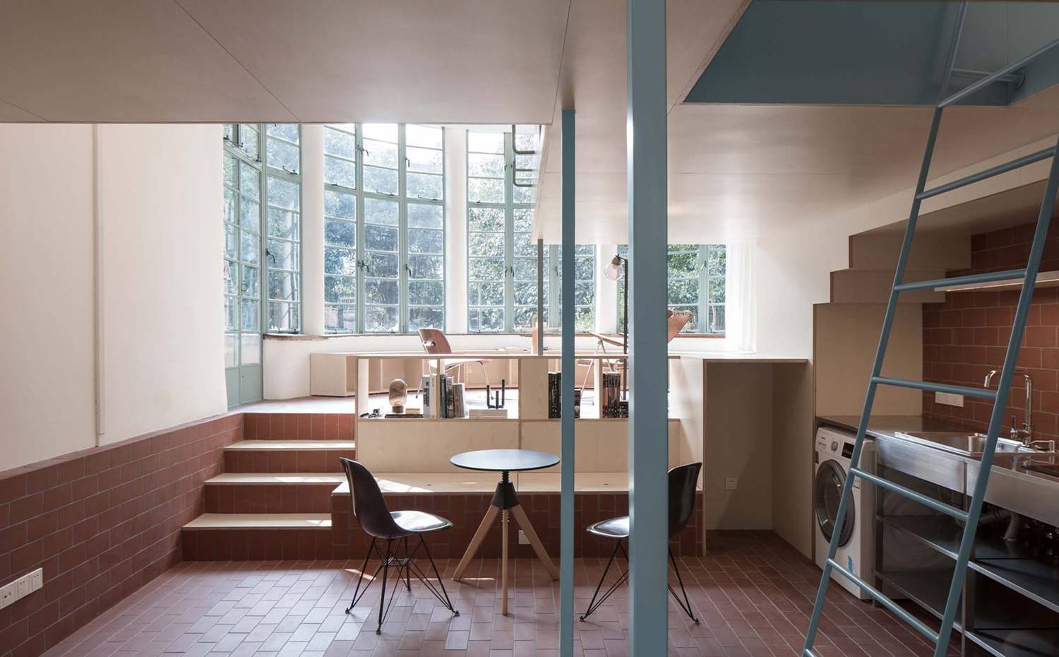 Zona de cocina y comedor con estructura de madera y metal. El mismo azul pálido que pinta la escalera interior se utiliza para los marcos de ventanas de metal exteriores.