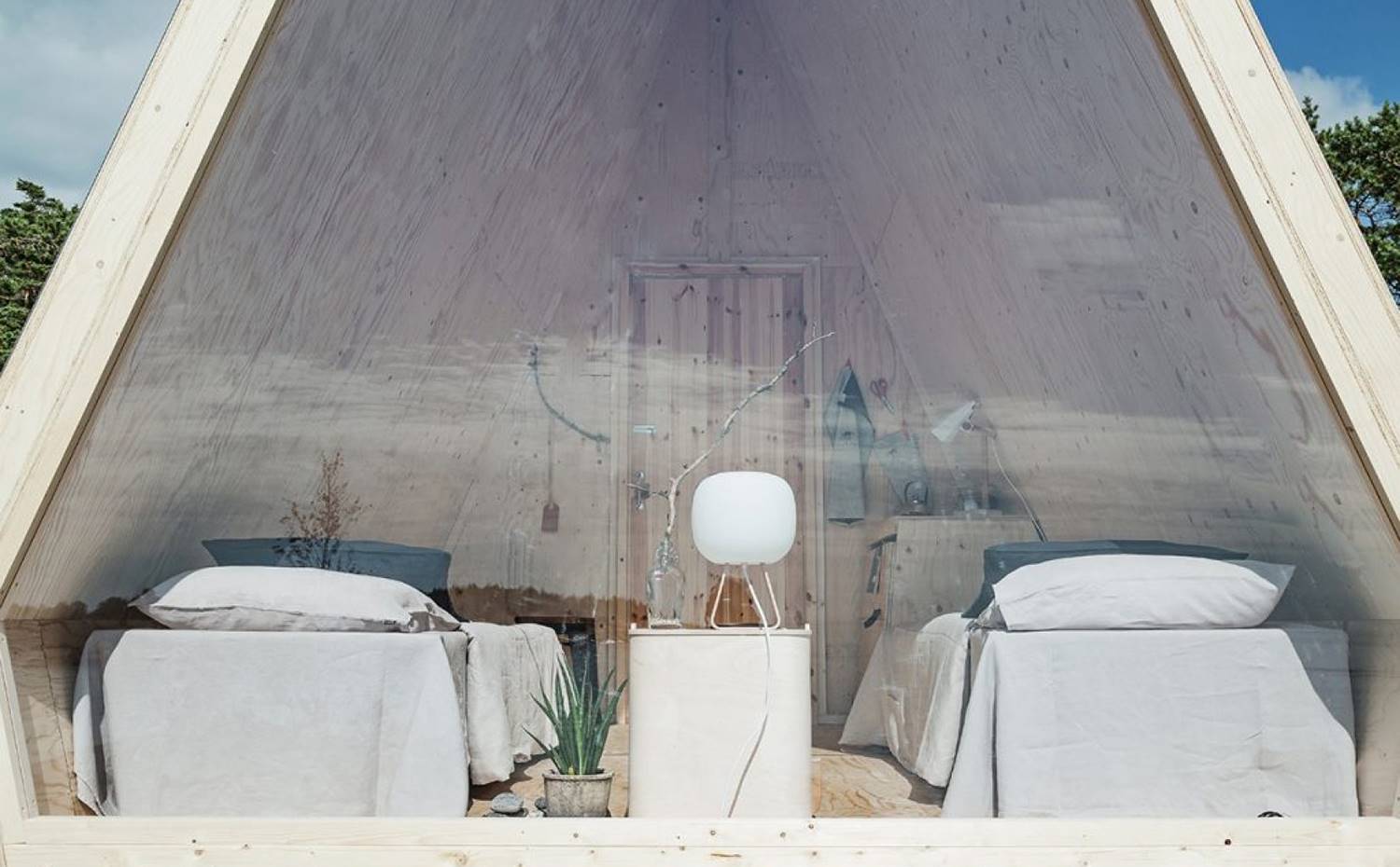 Camas, mesilla y lámpara de sobremesa del interior de cabaña. Falck se inspiró en la idea de acercar a las personas a la naturaleza con un impacto ambiental mínimo.