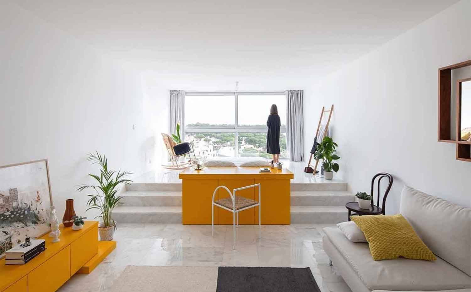 Salón con sofá blanco, mueble amarillo, escaleras a zona elevada dormitorio.. Una disposición diáfana, una depurada selección de piezas y una imponente entrada de luz natural, caracterizan a este pequeño apartamento de Vilamoura.