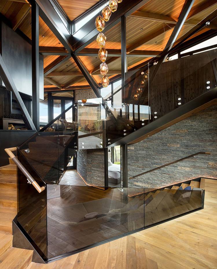 Zona de paso entre niveles, escalera con suelo y pasamanos de madera, lateral de cristal tintado, Lámpara suspendida de cubierta de madera y acero. Los espacios compartidos se organizan alrededor de la escalera abierta que conecta con los diferentes niveles de la vivienda.