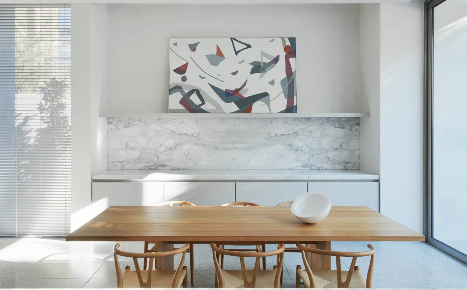 Cocina-comedor, mesa de madera, sillas de madera, frente de mármol, muebles bajos, cuadro en estantería. La dosis de calidez de la zona de día viene dada por la mesa y las sillas del comedor informal (y más funcional) de la casa, todo en madera natural. 