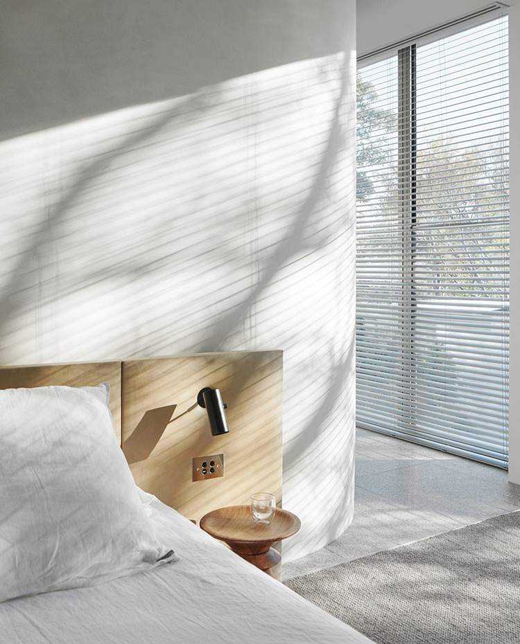 Dormitorio con cabecero de madera, iluminaria encastrada, cerramiento acristalado, cortinas de estor, tabique curvo. El dormitorio principal ha preservado la privacidad, ubicándose en la primera planta y concebido como una 'suite' de hotel, con vestidor y baño, separados por un muro curvo. 