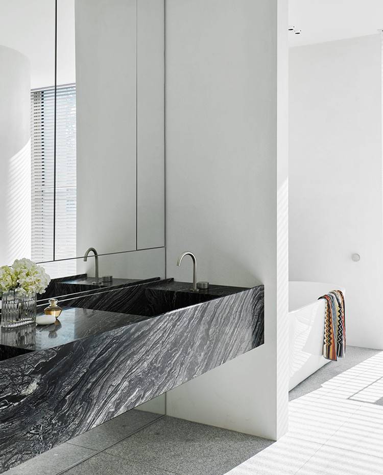 Lavamanos de mármol negro, grifería encastrada, bañera exenta, frente de espejo, suelo gresite gris. El baño del dormitorio principal cuenta con una encimera exenta de mármol negro con grifería encastrada que contrasta con el blanco puro de la bañera exenta.