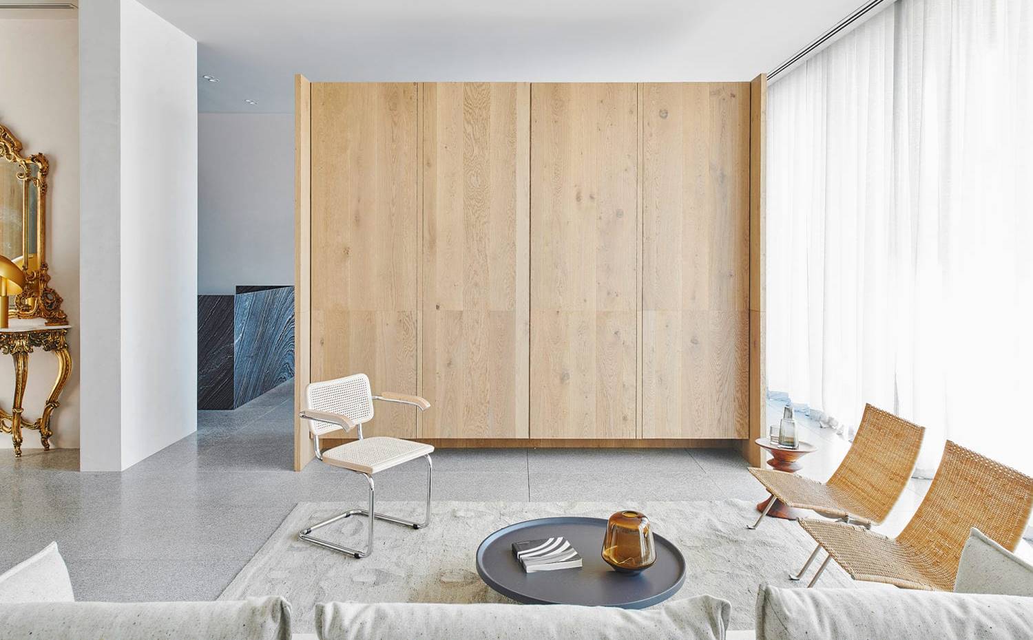 Salón, silla de fibra con brazos, bucatas de fibra, mesita de centro negra, armario de madera central. Esta unidad de carpintería independiente divide los salones y comedores, permitiendo que los espacios fluyan. 