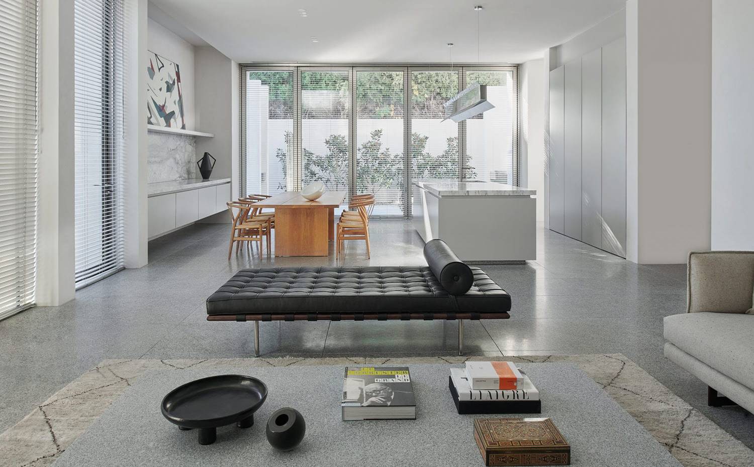 Salón.comedor y cocina en zona diáfana, claise-longue negra, mesa de centro. La zona de día se ha proyectado de forma abierta, dividida en zona de estar, las comedor y cocina con isla. La conexión con el exterior se hace a través de 5 grandes puertas pivotantes.