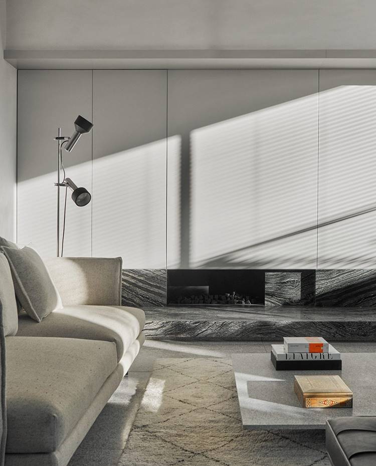 Sofá crudo, alfombra beige, mesa de centro gris, chimenéa con base de piedra, sobre mobiliario gris, lámpara de pie con dos focos. Esta sala de estar se ha concebido para que sus propietarios puedan relajarse en la familia, convirtiéndose en un punto de encuentro entorno a una chimenea y con dos sofás enfrentados para favorecer la comunicación.