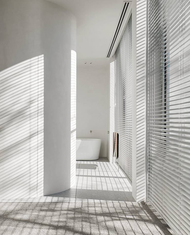 Zona de paso dormitorio-baño con tabique curvo, ballera exenta. El muro curvo que separa la zona de dormitorio del baño se decora con el juego gráfico de luces que inciden a través de los estores.