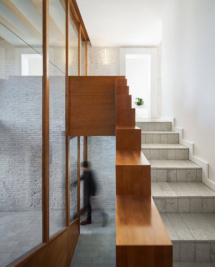 Escaleras revestidas de baldosa con estructura de madera, pared de ladrillo visto, cerramiento acristalado. La materialidad de la vivienda se ha logrado, desnudando y quitando todo tipo de adorno y acabado interior y devolviendo al edificio su aspecto original. 