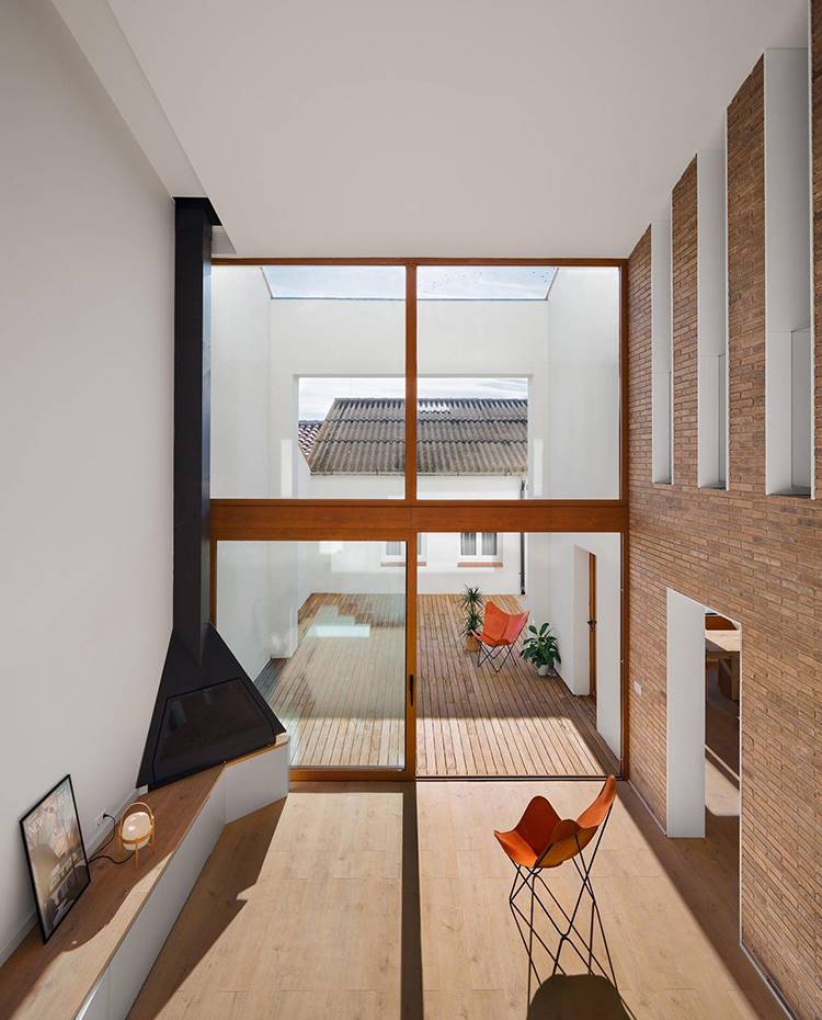 Salón abierto a un patio exterior de gran altura, con chimenea de acero en una punta, pavimento de madera, silla de piel con estructura modular. El estudio de arquitectura responsable del proyecto redujo la profundidad de los edificios originales para permitir que más luz natural penetrara hasta el centro de la casa.