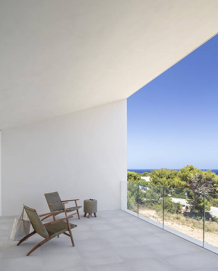 Terraza cubierta de hormigón con butacas de fibra y madera, puf de fibra y madera, vistas exterior islas. La pureza de líneas a base de hormigón da como resultado un edificio de estética robusta que mantiene la privacidad, a la vez que se abre al exterior y a sus panorámicas vistas a través de grandes aperturas. 