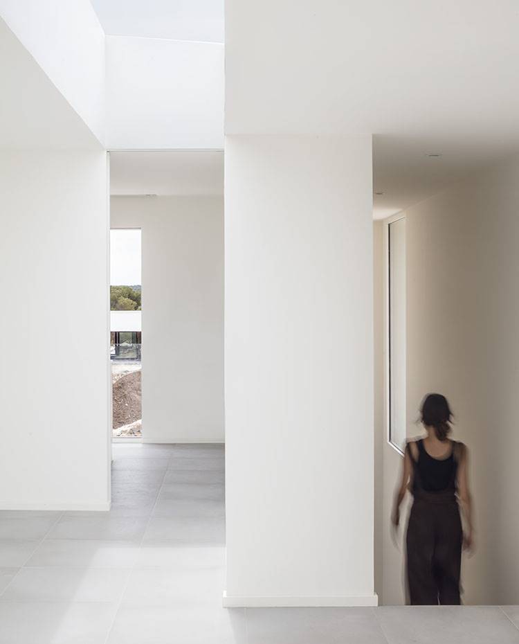Zona de paso interior de la vivienda, paredes blancas, lucernarios a gran altura. Un elemento prefabricado fue retirado del techo creando una gran claraboya que llena de luz natural el interior de la vivienda, especialmente en la parte posterior sin ventanas.