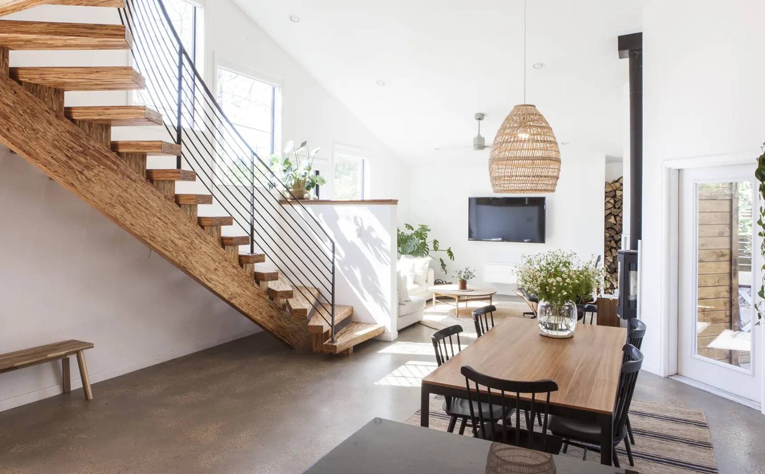 Comedor con mesa de madera y sillas negras, lámpara de suspensión de fibra, escaleras ondulantes con banco de madera en el hueco inferior.. El plano abierto de la sala de estar y la cocina hace que la energía sea realmente buena en la casa, favoreciendo la comunicación y la visión entre ellos mientras la familia desarrolla difentes tareas.