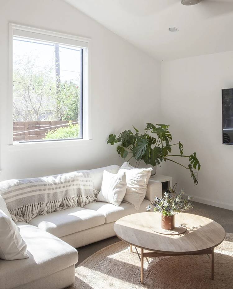 Salón con sofá rinconero, mesa de centro de madera, ventilador en techo inclinado, ventana a jardín. Para Shannon “ la vegetación hace una habitación”. Ya se trate de plantas de interior en macetas o un simple jarrón de eucalipto o manzanilla, “un poco de verde hace que un espacio, de repente, se sienta vivo y acogedor”.