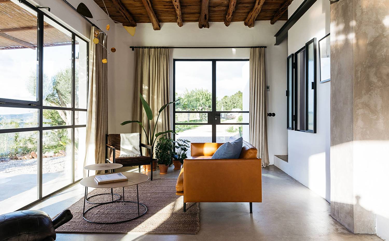 Sofá de piel, mesitas auxiliares circulares, alfombra de fibra, viga de hierro, chimenea elevada en obra, cerramientos de cristal.. El salón, equipado con un mobiliario de carácter urbano, comparte espacio junto al comedor y la cocina, todos ellos conectados a una amplia terraza privada, que ofrece vistas espectaculares del valle. 
