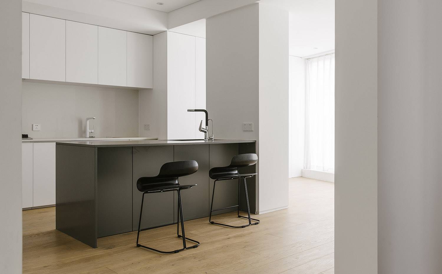 Cocina con office, taburetes negros, suelo de madera, mobiliarop en blanco, aperturas tabiques, focos en techo. La combinación de muebles blancos, para el frente de pared, y grises, para la zona de office, caracteriza a la cocina, que cuenta con generosas aberturas hacia espacios contínuos, contribuyendo a la entrada de luz natural.