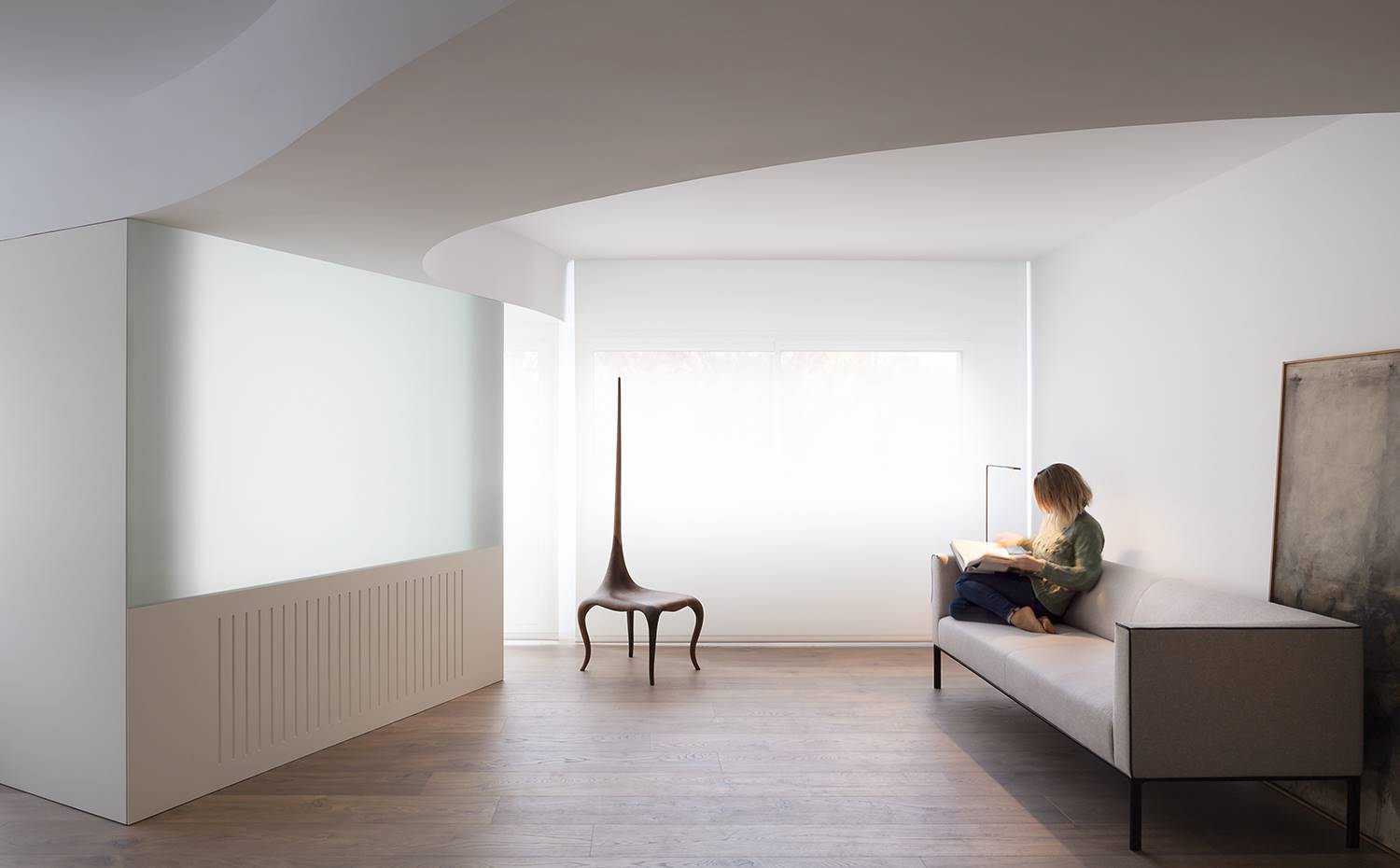 Salón con sofá gris, suelo de madera, silla-escultura modernista, techos ondiulados. El proyecto de reforma realizado por el estudio valenciano Balzar Arquitectos contempla la renovación completa de una vivienda cuya planta presentaba distintos paramentos que originariamente no eran perpendiculares entre sí.