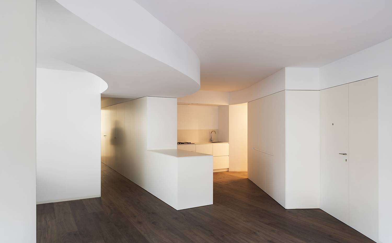 Zona cocina abierta al comedor, línea de armarios divisorios, techos ondulantes. La distribución dibuja un espacio continuo en el acceso, con la cocina abierta al comedor y al salón. Ahora bien, su configuración la sitúa en una zona reservada de la planta, ajena a miradas indiscretas mientras se está cocinando.