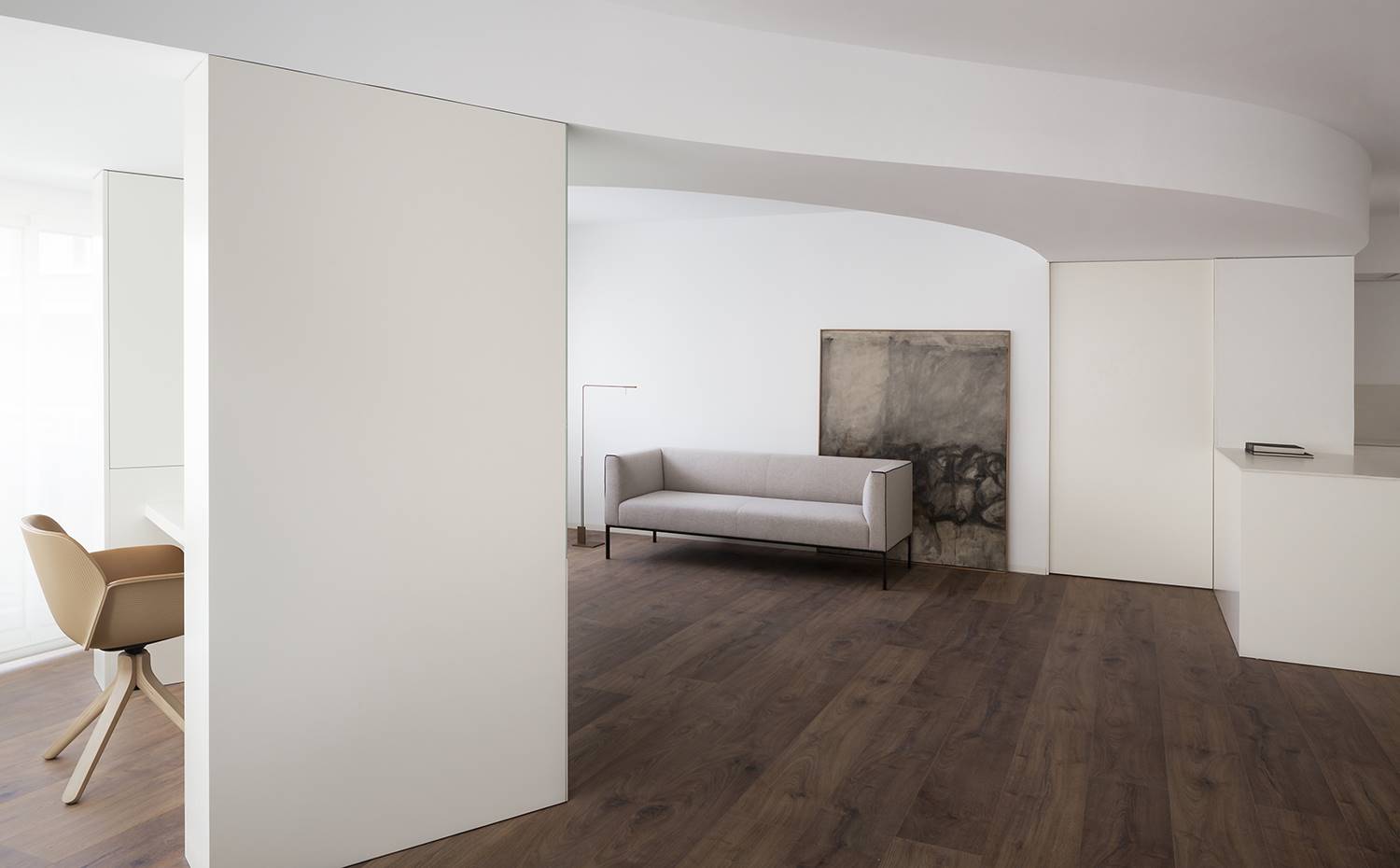 Zona de trabajo tras estructura de madera lacada en blanco, puerta corredera hacia dormitorios. Un tabique translúcido delimita el antiguo balcón, ahora convertido en zona de trabajo. Está integrado en una estructura que soporta tanto el escritorio como esconde dos columnas de acero.