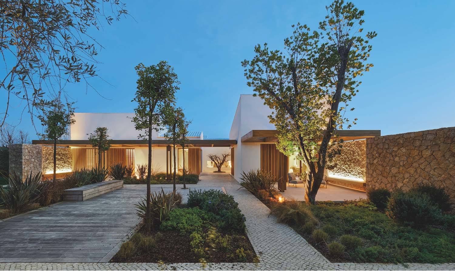 Vista exterior de Casa Da Rocha. Existen distintos niveles de privacidad en el uso del espacio, distinguiendo ambientes recogidos y con aberturas bajas para su uso estival. Esta parte del jardín se ha pavimentado con tarima flotante de lamas de iroco y teselas de piedra calcárea.