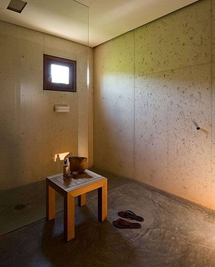 Baño con suelo de pizarra, ducha con mampara de ciristl y plato integrado. Taburete de madera y zapatillas de plástico. La privacidad también se ha respetado en el baño, donde la luz natural incide en la justa medida para jugar con las diferentes texturas que revisten un espacio díafano libre de artificios.