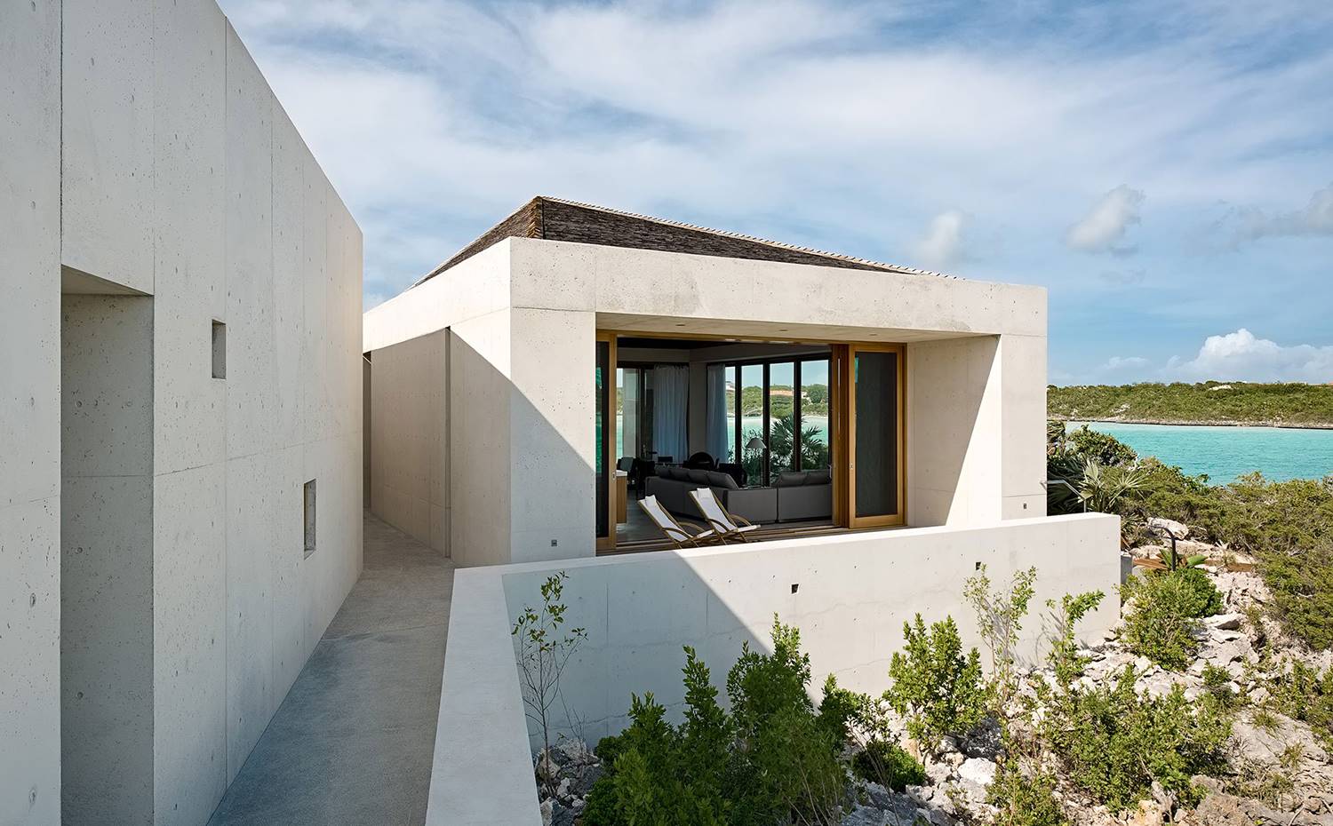 Fachada de hormigón, murete hacia peñasco, tumbonas junto a comedor. Pasillos estrechos para conducir la brisa marina y cortes geométricos para hacer lo propio con la luz natural, se suceden a lo largo de un proyecto de líneas puras. 