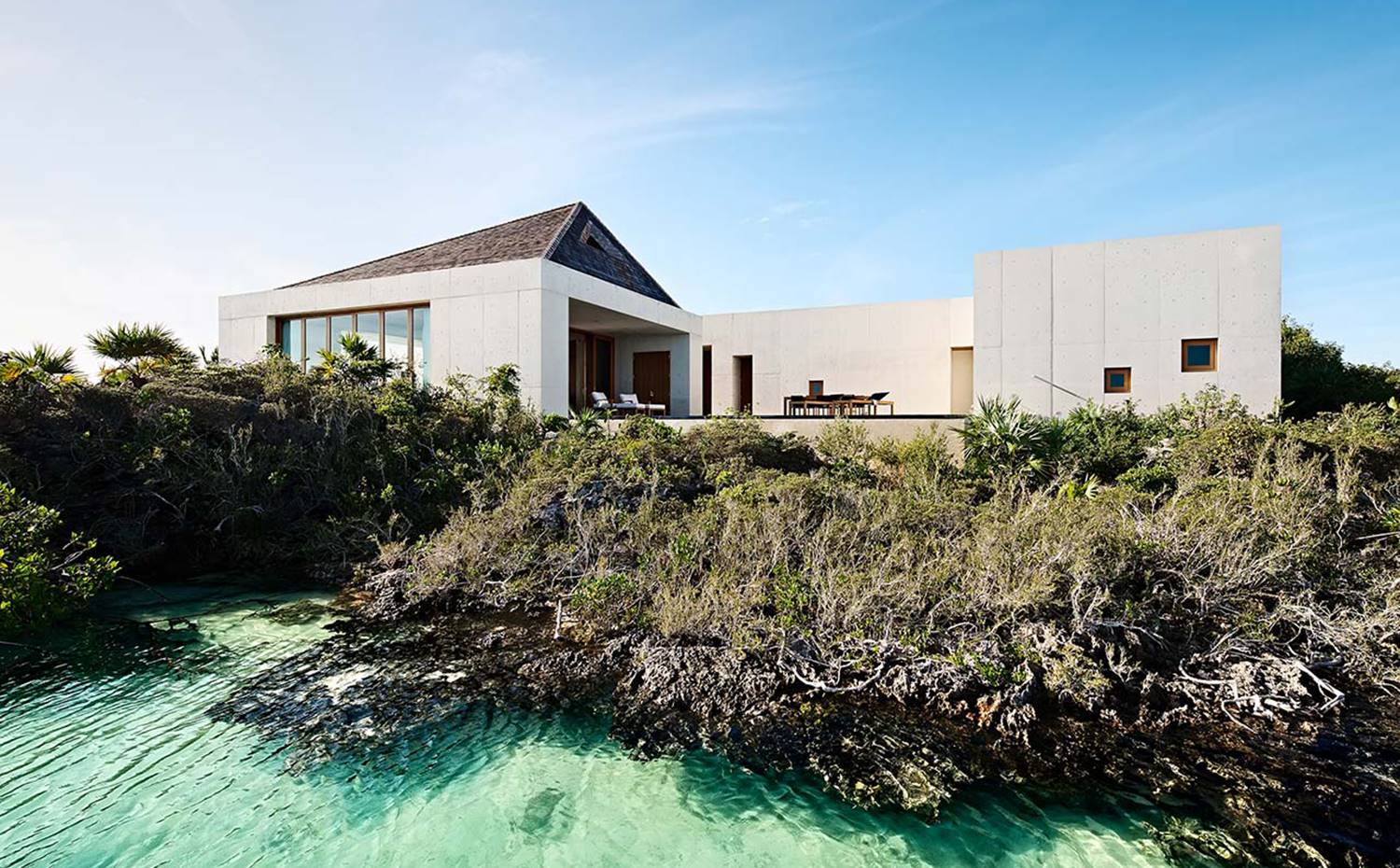 Fachada exterior con dos módulos y una zona central desubierta. Vegetación y agua en primer término. La distribución de la vivienda es tan simple como singular, donde una terraza de generosas dimensiones sirve de enlace entre las áreas más privadas, situadas al oeste, y el pabellón de la zona de día, al este.