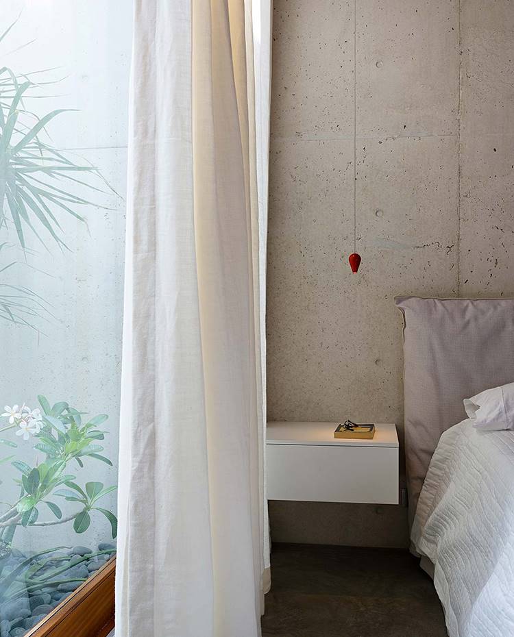 Mesita de noche suspendida en pared de hormigón, lámpara suspensión con cabeza color rojo, tamaño mini. En el dormitorio, las luces que cuelgan sobre las mesillas suspendidas y las cortinas de lino que ondean suavemente con la brisa del océano, realzan aún más el ambiente zen de la casa. 