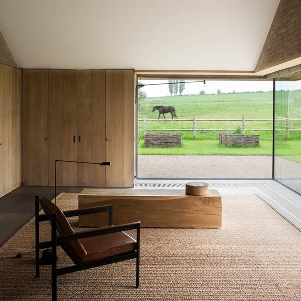 Alfombra de tejido natural, banco de madera y sillón de cuero. Casa en Zwevegem de Vincent Van Duysen.