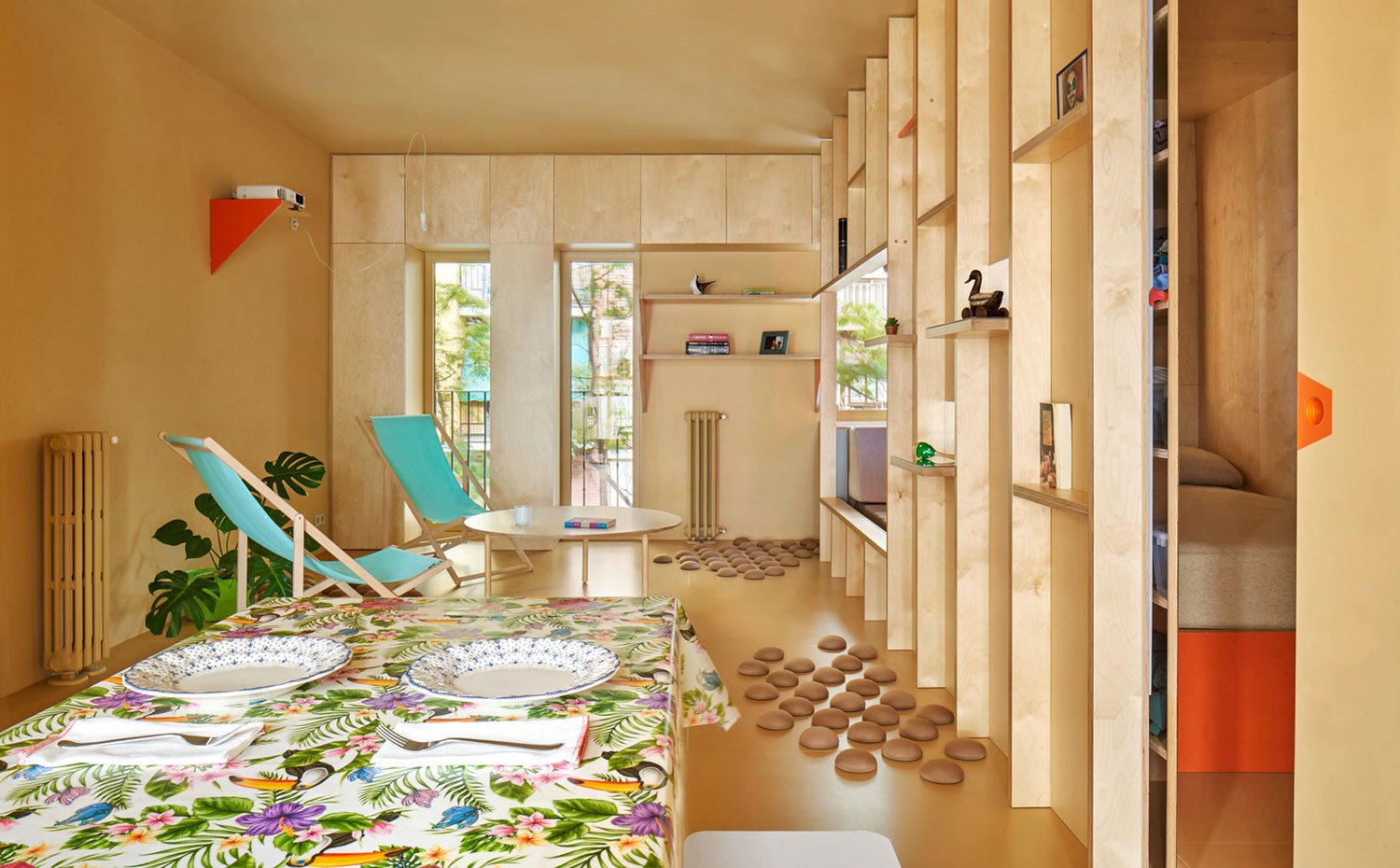 Comador con mantel de flores, tumbona tela verde y estructura de madera, mesa de centro madera, estructura lateral vivienda