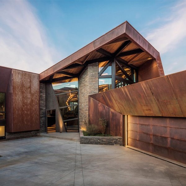 Estructura exterior vivienda de acero corten y miedra, entrada con cerramientos de cristal y madera.