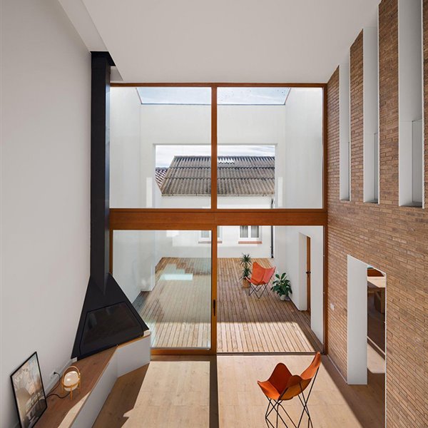 Salón abierto a un patio exterior de gran altura, con chimenea de acero en una punta, pavimento de madera, silla de piel con estructura modular