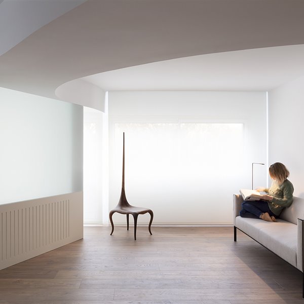 Salón con sofá gris, suelo de madera, silla-escultura modernista, techos ondiulados