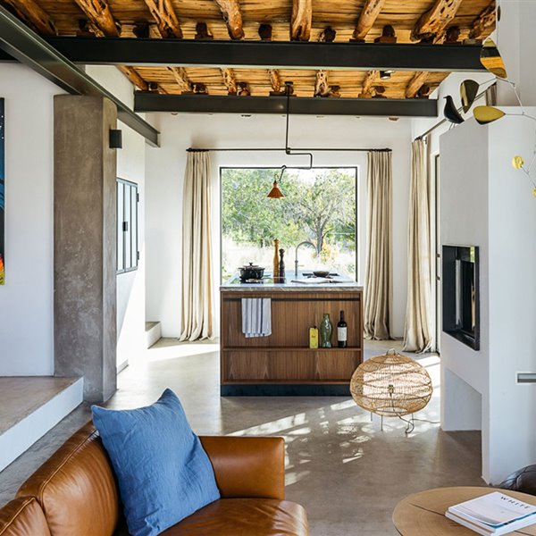 Zona comedor y salón, lámpara de suelo de fibra, sofá de piel marrón, cojín azul, revestimientos y suelo de hormigón, cortinas de lino en cerramientos, vigas de hierro