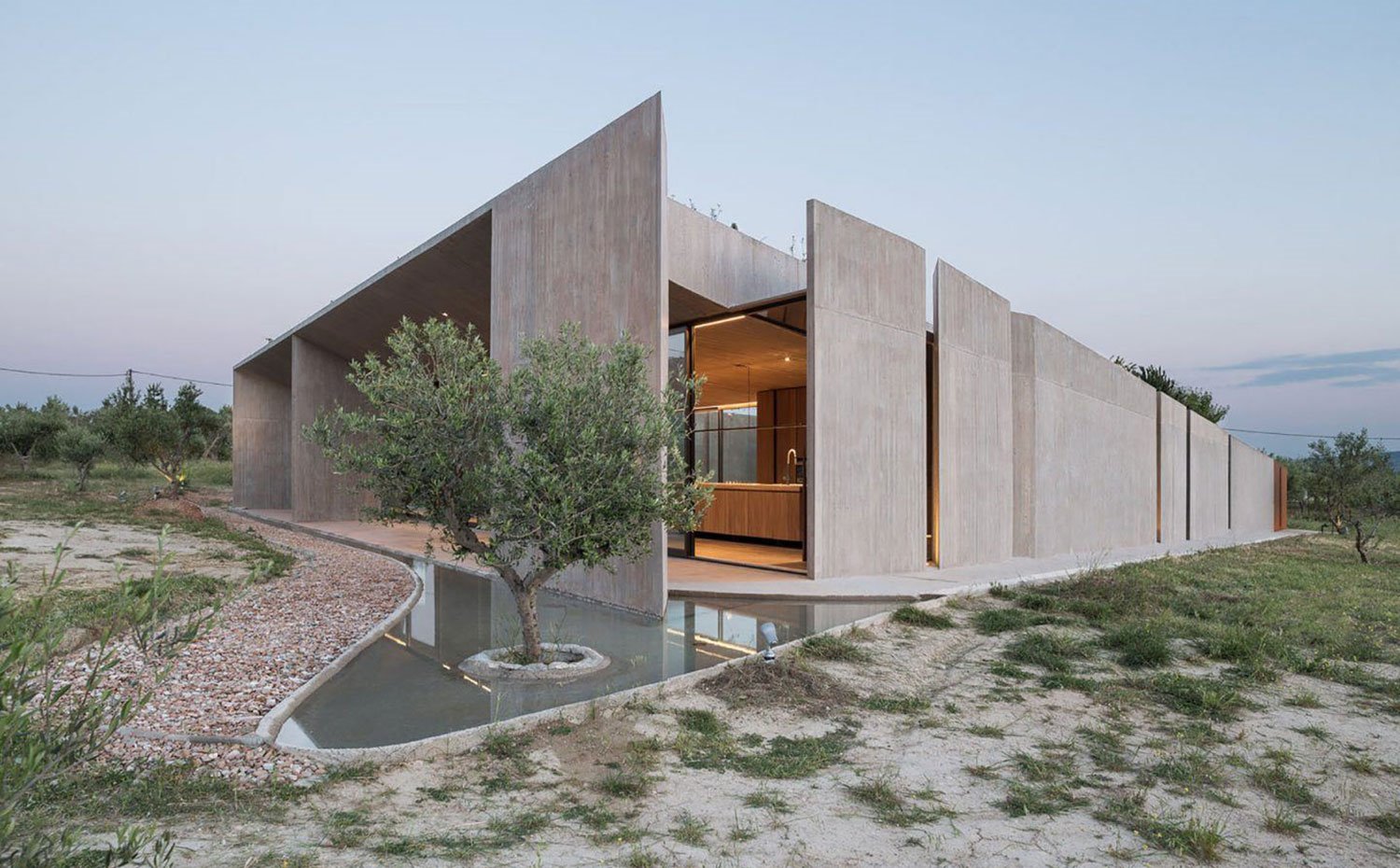 Exterior estructura con bloques de hormigón, arbol en esquina con agua, interior cocina iluminada