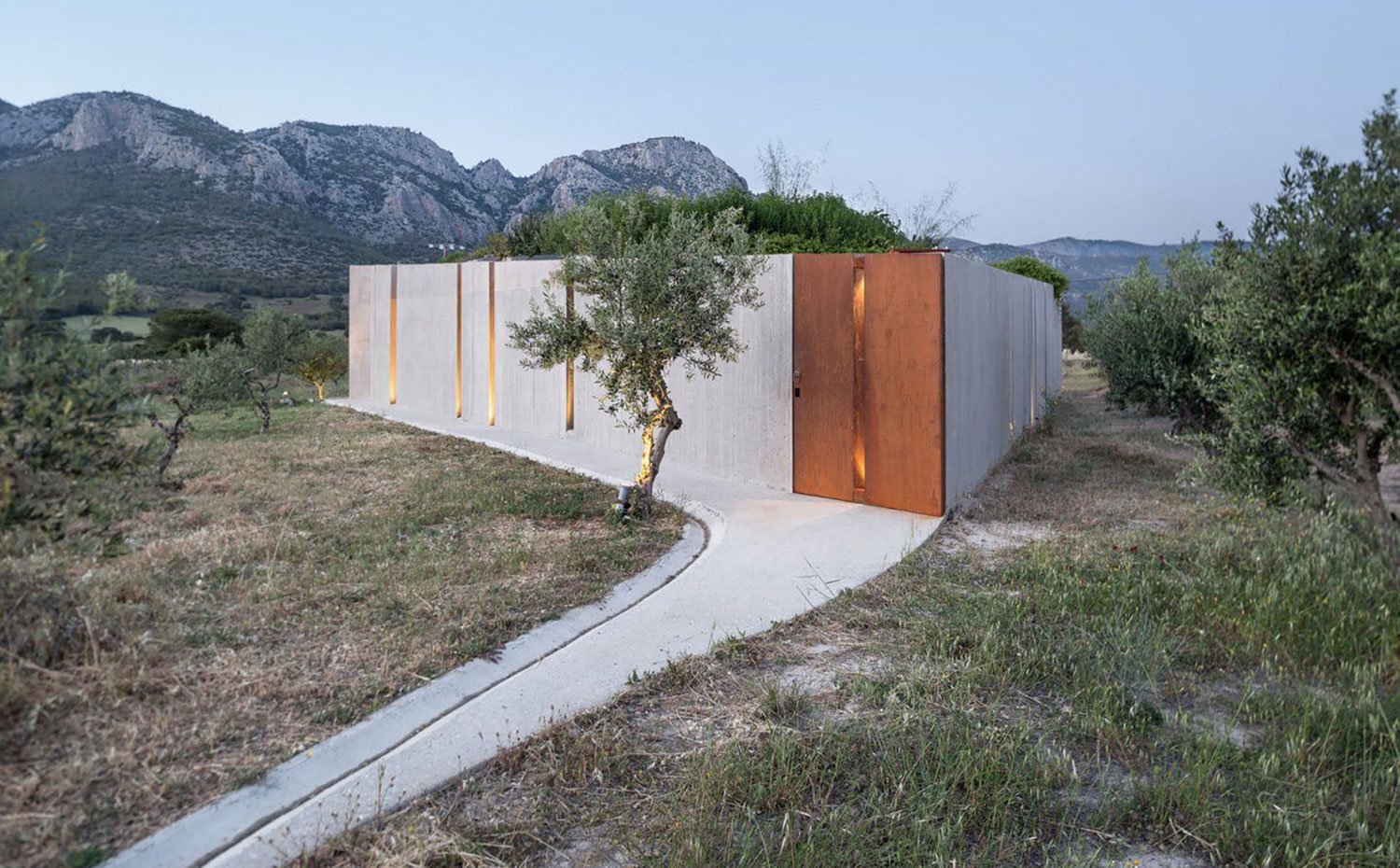 Parte trasera de casa, exterior roddeado de árboles y zona rural, estructura de hormigón y hoja de acero corten.
