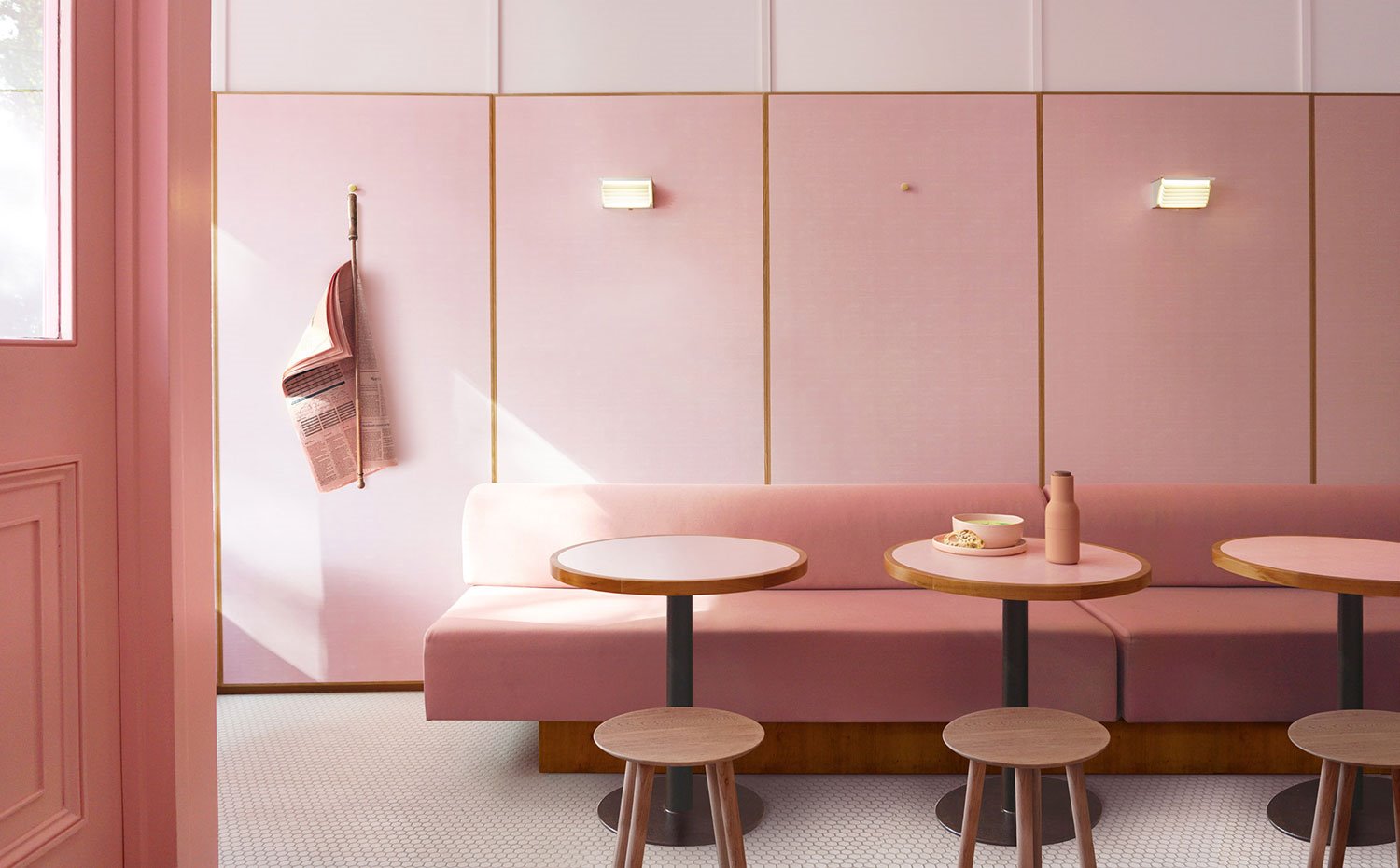 Banco corrido tapizado en rosa con base en madera, mesas circulares con base cromada, suelo de gresite, apliques pared, taburetes madera, diario colgado en pared