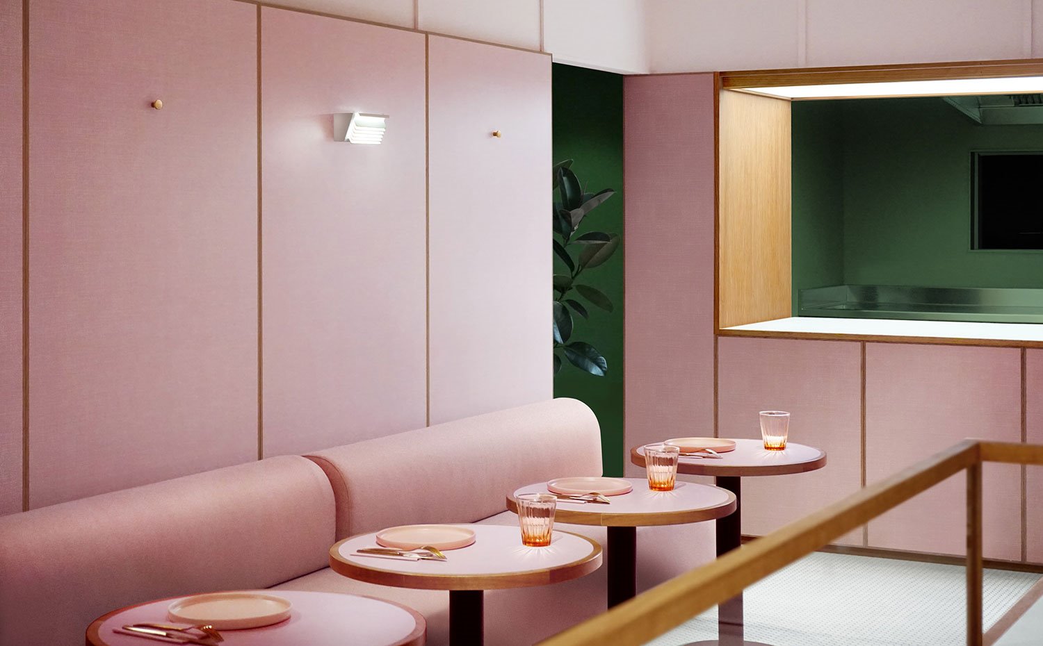 Cocina abierta con pared en verde, estructura pasaplatos en rosa y madera, bancos tapizados en rosa, mesas circulares en rosa con vasos de cristal y vajilla color salmón, apique en pared