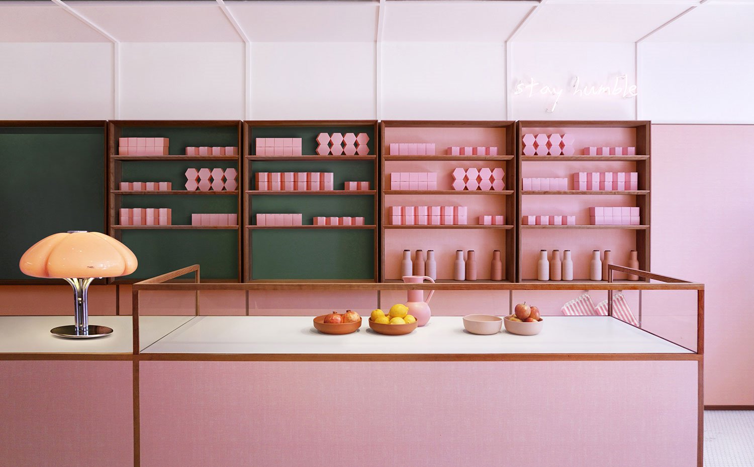 Mostrador en rosa, lámpara de sobremesa con pantalla de cristal, bols con fruta, estanterías con frente verde y rosa, embases en rosa