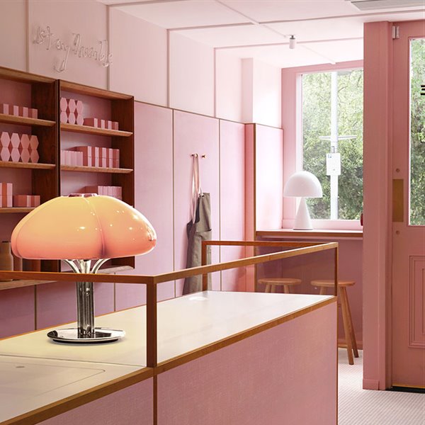 Mostrador en rosa, lámpara de sobremesa con pantalla de cristal y pie cromado, puerta en madera rosa y cristal, escaparate con taburetes de madera, delantal colgado