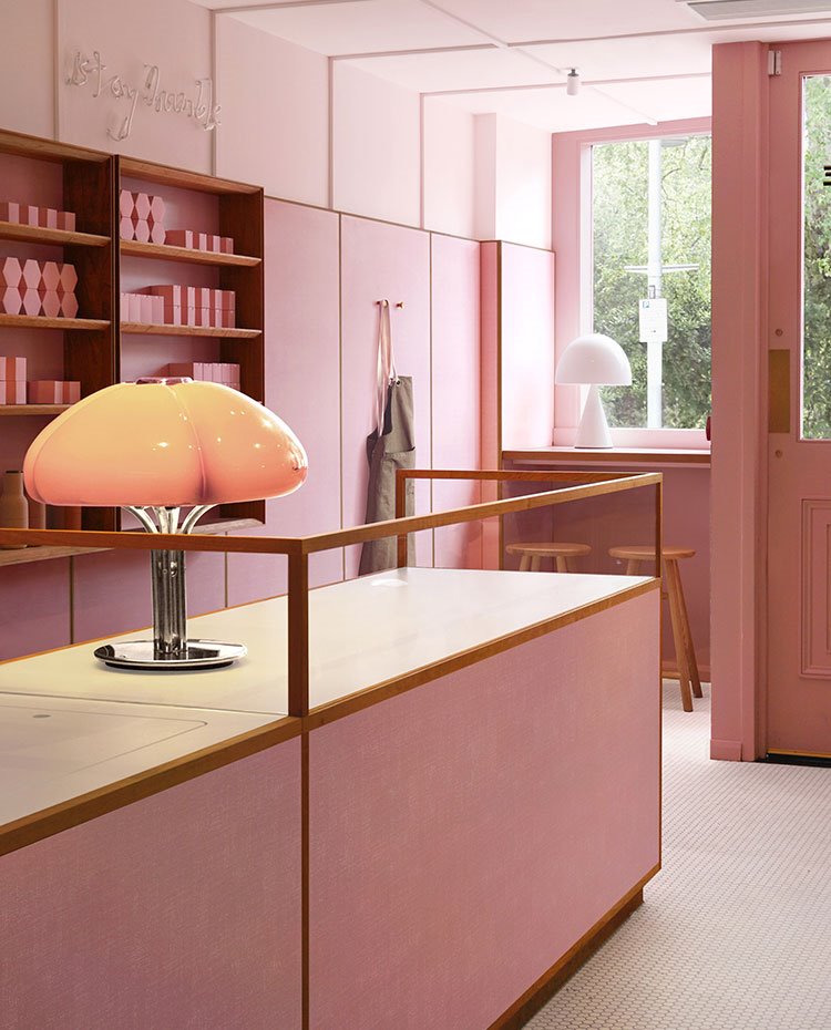 Mostrador en rosa, lámpara de sobremesa con pantalla de cristal y pie cromado, puerta en madera rosa y cristal, escaparate con taburetes de madera, delantal colgado