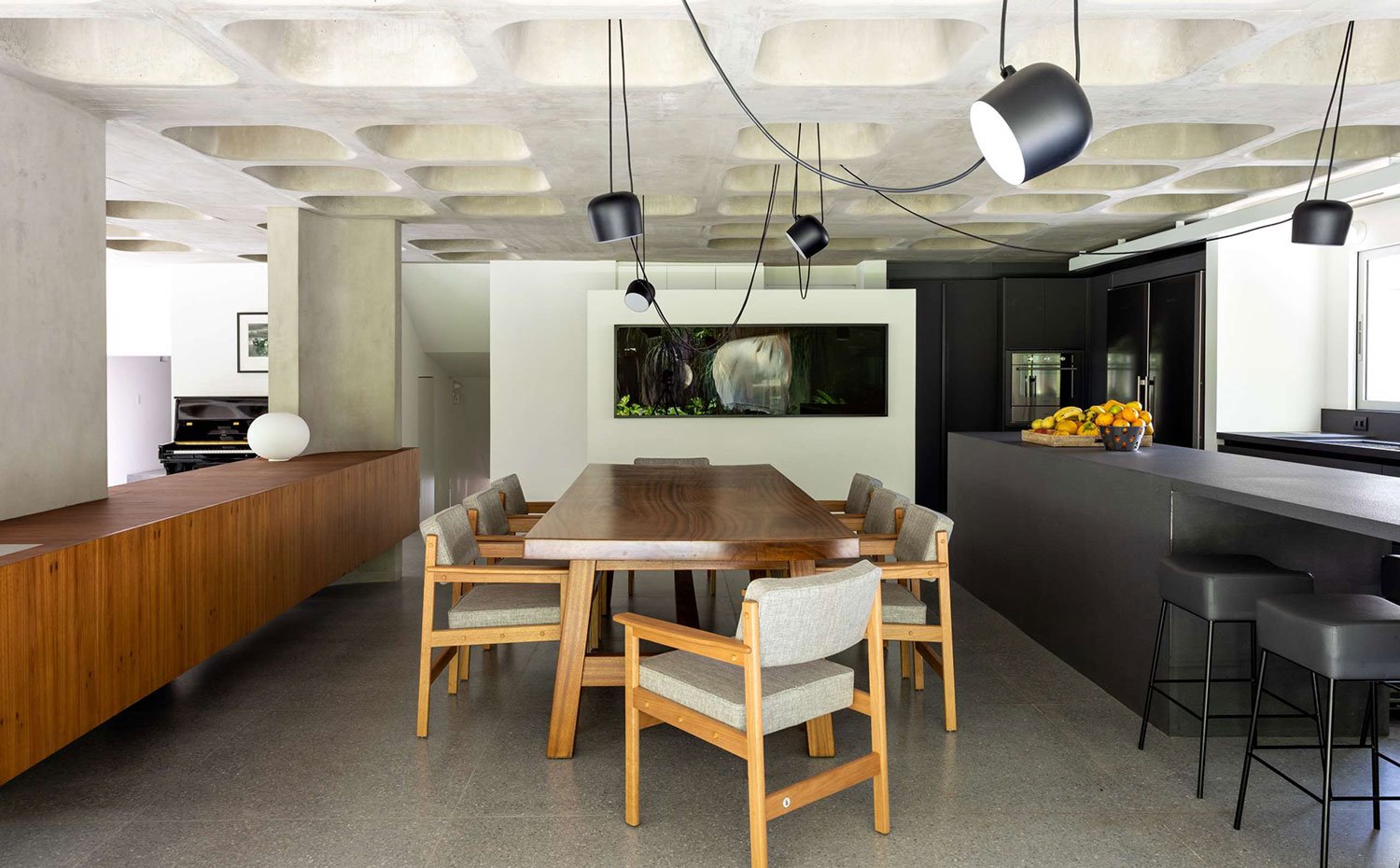 Comedor-con-sillas-madera-tapizadas-en-gris,-mesa-de-centro-rectangular-de-madera,-lámparas-suspendidas-en-negro-con-cableado-a-la-vista