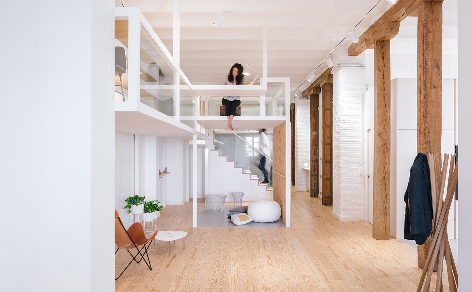 Vista-salón-en-dos-niveles,-espacios-abiertos-con-estructura-en-acero-y-madera,-suelo-de-madera,-perchero-de-madera,-butaca-marrón-con-estructura-tubular,-viga-y-pilares-de-madera