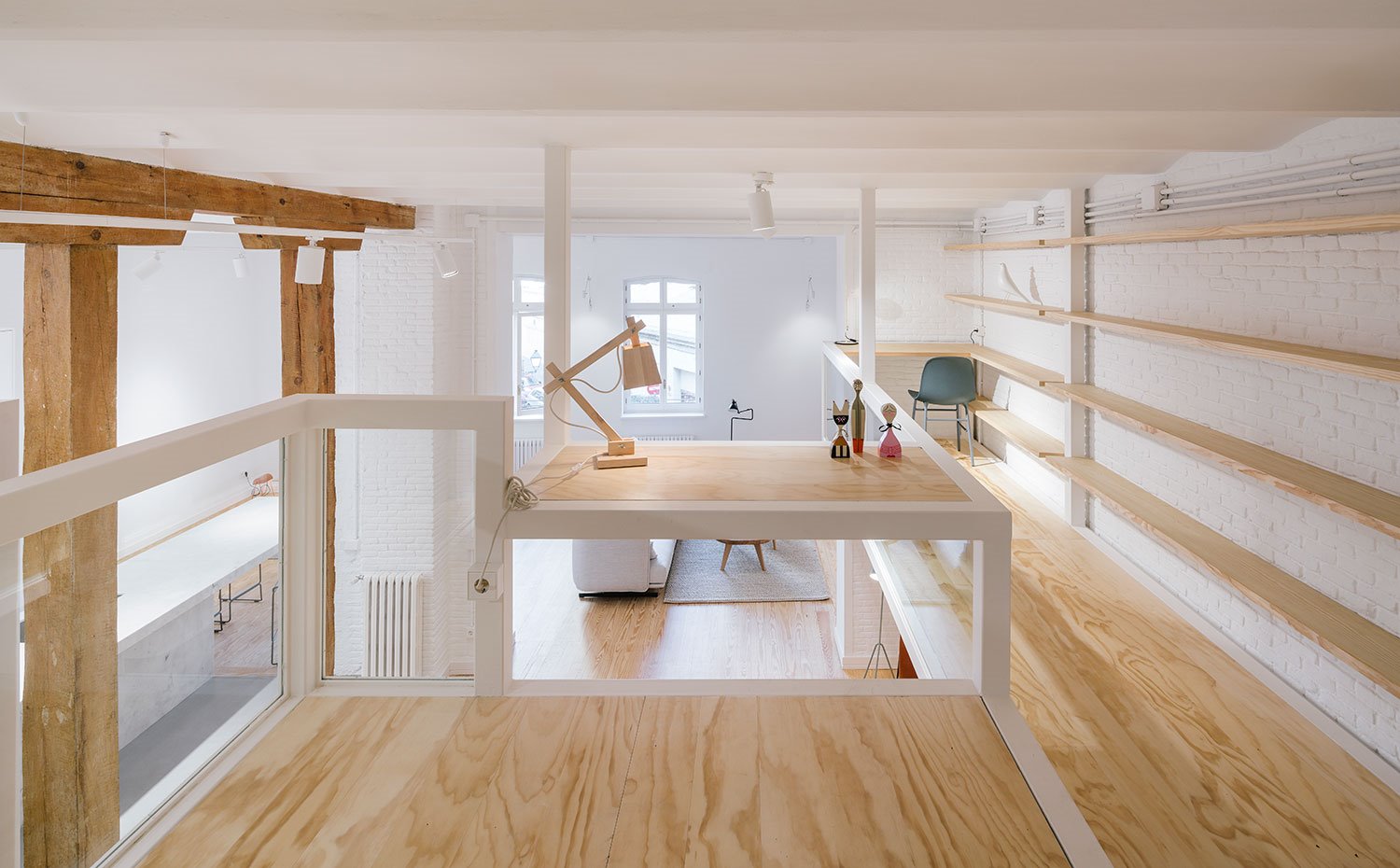 Zona-de-trabajo-en-nivel-superior,-estructura-de-hierro-blanco-y-madera,-lámpara-de-sobremesa-de-madera,-foco-iluminación-techo,-baldas-en-pared,-rincón-mesa-de-trabajo-con-silla-en-gris
