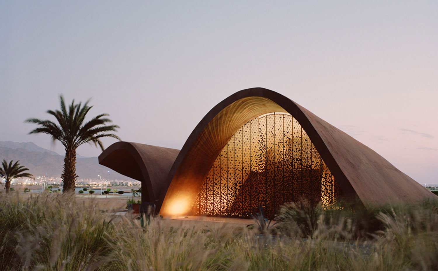 Estructura-ondulante,-hoja-de-acero-corten-perforada,-vegetación-anterior,-palmera,-luz-encendida