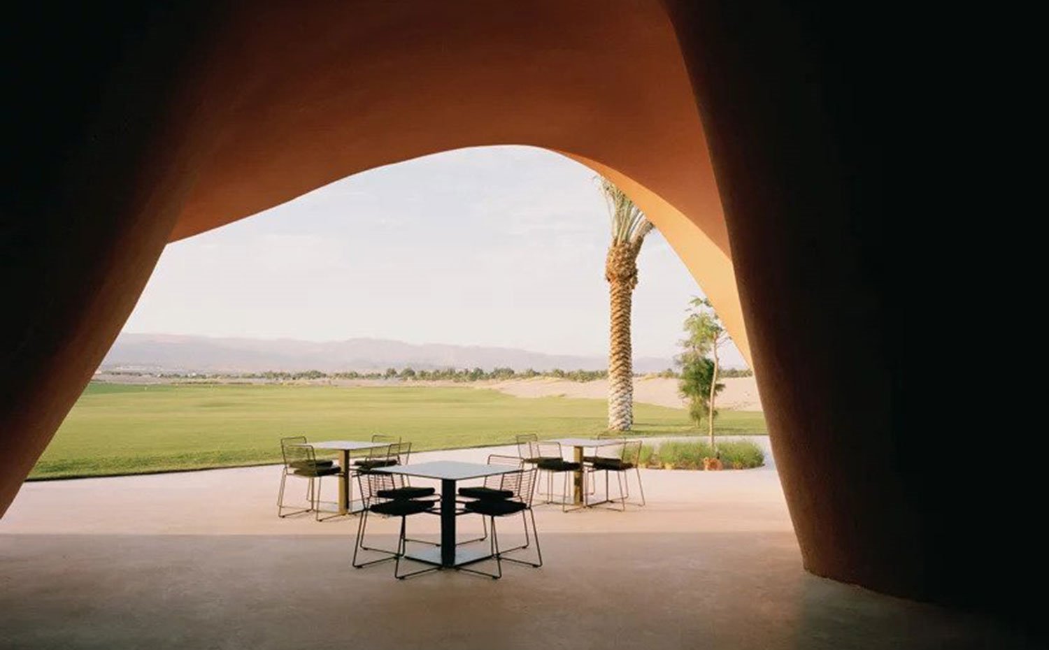 Mesas-y-sillas-en-exterior-junto-a-estrucura-ondulante-y-zona-de-golf
