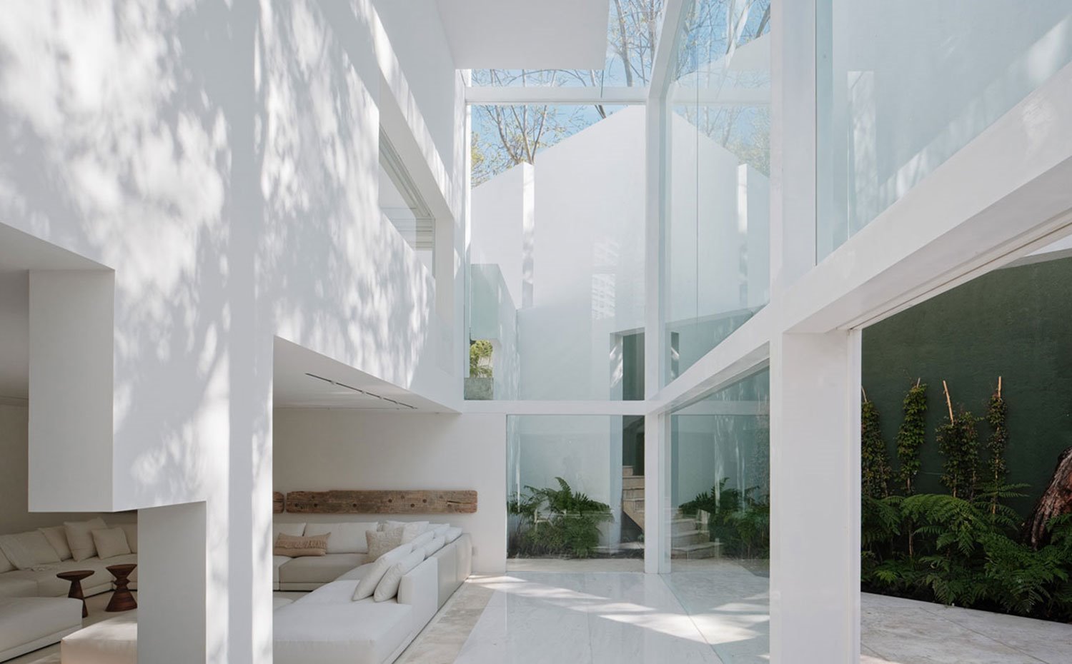 Cerramientos de cristal, estructura de marcos en blanco, salón abierto, sofás blancos en combinación con conjines y módulos crema, mesitas de madera, exterior con vegetación