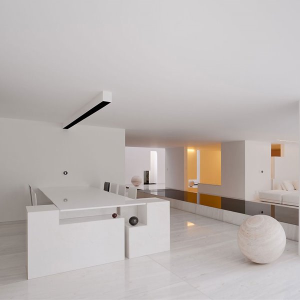 Comedor con estructura rígida en extremo y sillas a juego en blanco, iluminación de techo, esfera de piedra, pasarela decorativa con sobre en negro, salón con sofás en blanco