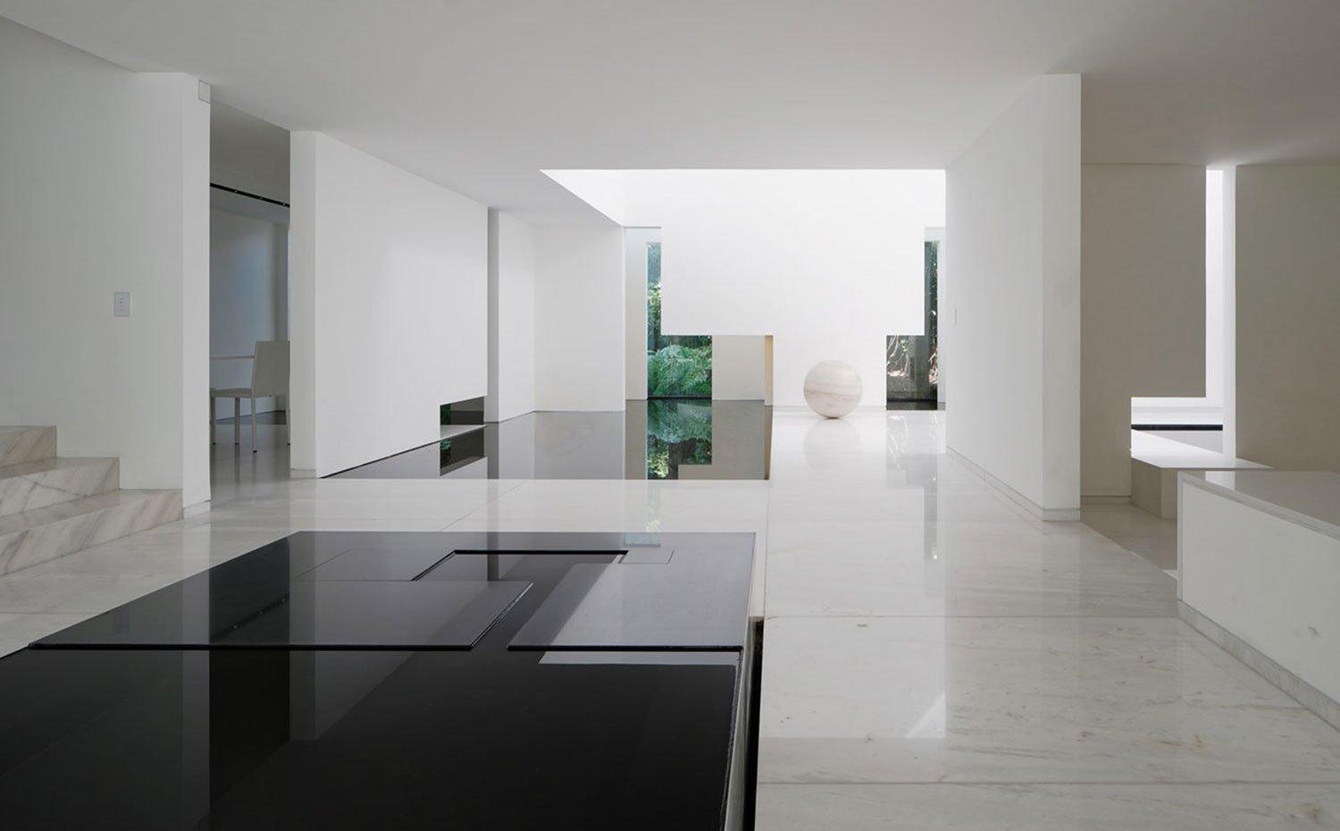 Sala con suelo de marmol, sobre de mesa negro, paredes en blanco, superficie de agua, esfera de mármol