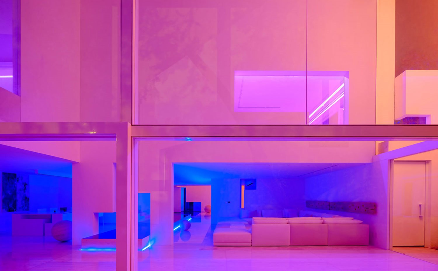 Vista exterior de interior con iluminación con neones, aperturas geométricas, paredes en blanco con reflejos de colores
